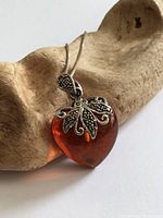 Front view of amber heart pendant on snake chain resting on driftwood