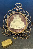 Front view of brass filigree frame with photo, wind-up musical box in foreground