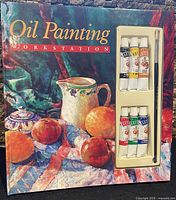Front of sealed Oil Painting Workstation kit showing book cover art, paint tubes, brush