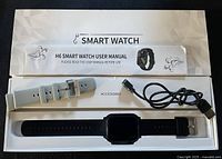 Box interior showing H6 smartwatch with black band, grey spare band, USB charger, manual