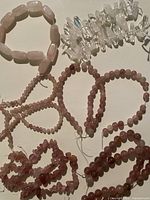 Multiple pink strawberry quartz strands, rose quartz rectangular bead strand formed into a loop, and clear quartz chip strand displayed on flat surface