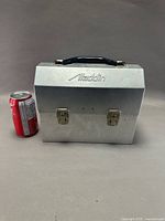 Front view of closed aluminum lunch box beside cola can for scale