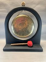 Front view of brass gong in black wooden stand with mallet