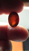 Oval deep orange-red garnet held between fingers