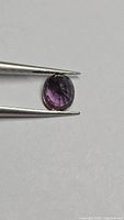 Oval faceted deep purple sapphire held by tweezers on neutral background