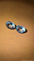 Two oval aquamarine gemstones on brown surface