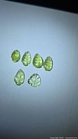 Six yellow-green leaf-cut tourmaline stones on neutral background