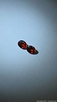 Two oval faceted burnt orange garnets on light background
