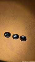 Three oval black cabochon gemstones on brown background