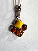 Front view of pendant hanging from chain showing amber stones and bail