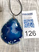 Front view of blue agate pendant on cord with lot tag