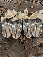 Four aluminum scoops with ribbons displayed on patterned surface