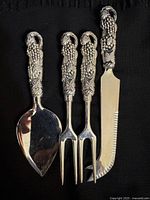 Full view of four ornate handled serving utensils on black background