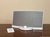 Front view of white Bose SoundDock speaker dock with remote placed to the left