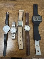 Group shot of five wristwatches laid out on wood surface