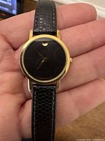 Front view of Movado watch showing black dial, gold bezel, leather strap