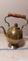 Full view of brass teapot showing pedestal base, spout, wooden handle and finial