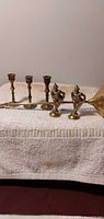 All six brass items grouped: three candlesticks, two figurines, one candle snuffer
