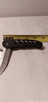 Closed knife against tape measure showing 3.5-inch handle, black handle with holes
