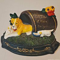 Front view of painted cast iron doorstop showing dogs, barrel, floral accents, and inscription