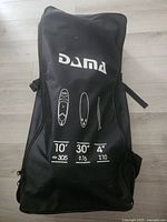 Front of sealed DAMA backpack showing brand and board dimensions