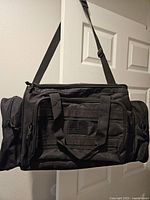 Front view of black Highland Tactical duffel showing handles, shoulder strap, front pocket and webbing