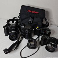 Overview showing two digital cameras, compact camera, two lenses and camera bag