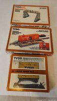 Three boxed Tyco items: crossover bridge, operating boxcar, power pack