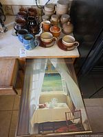 Stoneware canisters, mugs, cups/saucers on counter with framed print partly visible