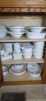 Cabinet shelves showing majority of CorningWare French White pieces stacked