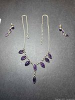 Full view of necklace and both earrings on dark background