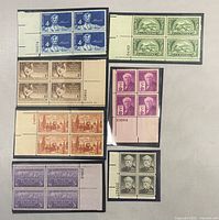 Front view of all seven US stamp blocks showing designs, denominations and plate numbers