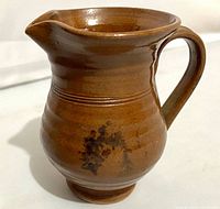 Side view of brown glazed redware pitcher with handle and ribbed body