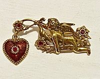 Front view of gold-tone cherub brooch with red rhinestones and heart charm
