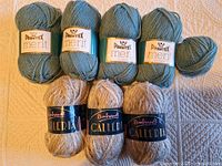 Three full skeins and one partial skein of Phentex Merit teal yarn, three skeins of Rembrandt Galleria beige fleck yarn displayed on surface