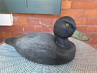 Full view of wooden duck decoy on wicker table