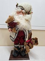 Full view of Santa figurine holding teddy bears on wooden base