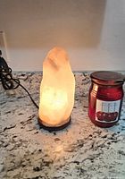 Salt lamp illuminated beside red jar candle