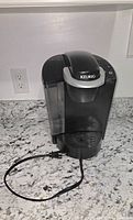 Front view of Keurig brewer showing water reservoir, drip tray and cord