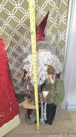 Full view of Santa figurine beside folded table runner with tape measure showing height