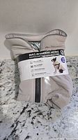 Folded beige dog jacket in packaging showing front zipper