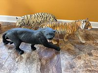 Three porcelain big cat figurines displayed together on tile floor