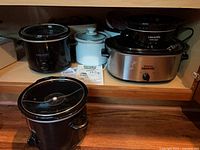Shelf with five slow cookers of various sizes and colors