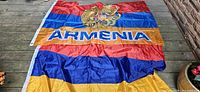 Full view of one flag laid flat showing stripes, coat of arms, lettering, grommets