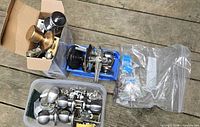 Overview of lot showing boxed knob set, blue bin with keyed locksets, clear tub of satin nickel knobs and zip bag of parts