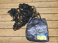 Coiled black cargo net alongside its black storage bag on wood surface