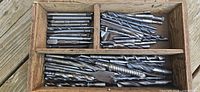 Open wooden box showing multiple drill bits in two compartments