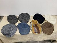 Eight flat caps laid out showing variety of colours and fabrics