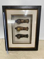 Front view of framed shadowbox showing three door-knob castings and ruler for scale