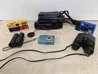 Group shot of all items: camcorder, digital camera, two disposable cameras, two binoculars
